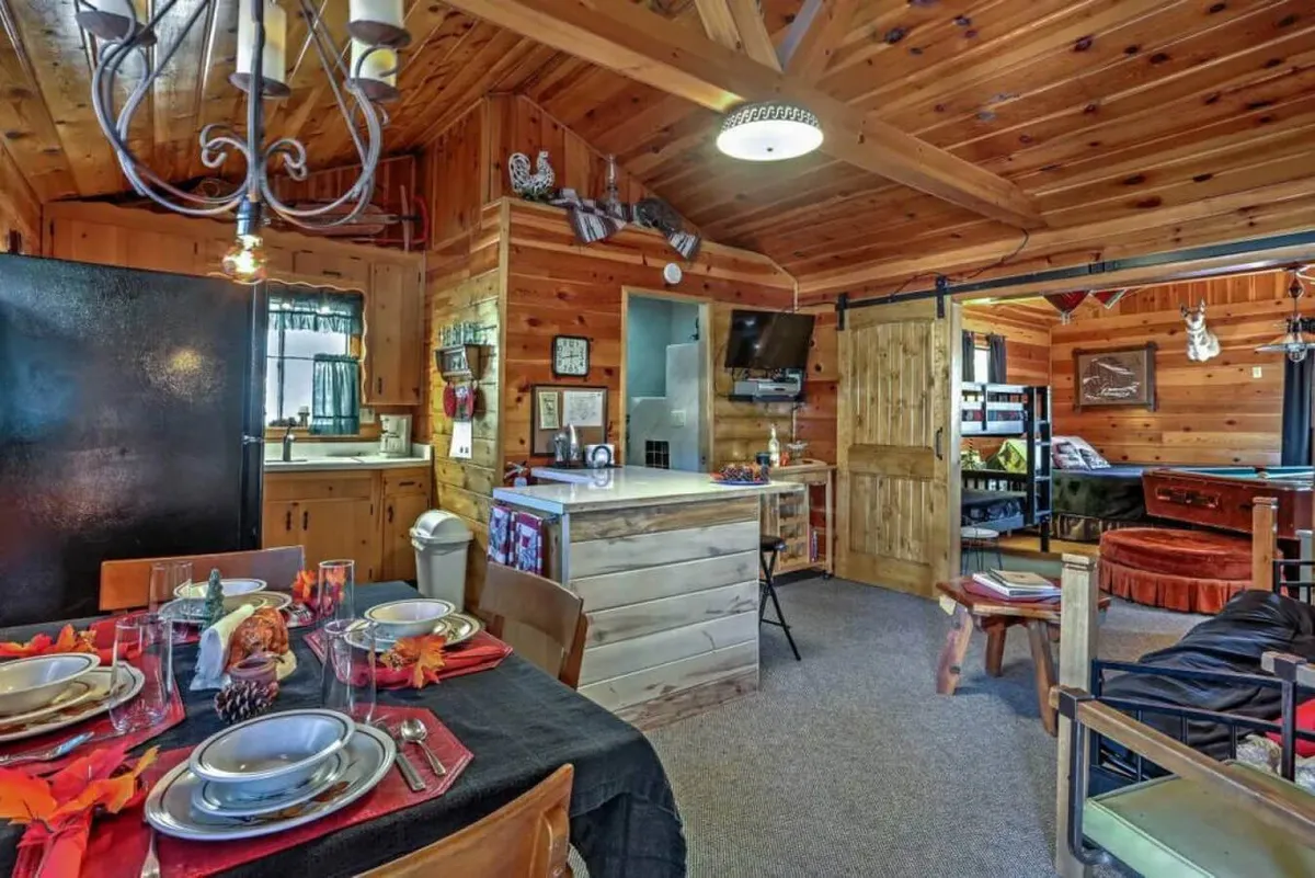A dining area with a wooden table set for a meal, kitchen area visible in the background, wooden accents throughout, and cozy bunk beds at the back. The arrangement encourages family meals, game nights, and lively conversations.