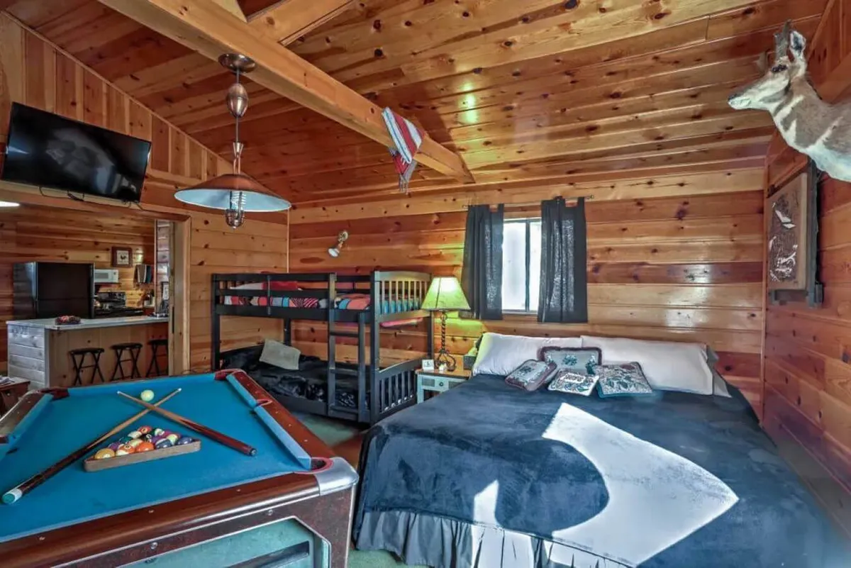 A welcoming space with a pool table, bunk beds, a comfortable queen bed, and warm wooden walls. The mounted deer head adds a touch of rustic charm. The room is designed for both relaxation and fun, with ample space for group activities including playing pool, watching TV, and socializing.