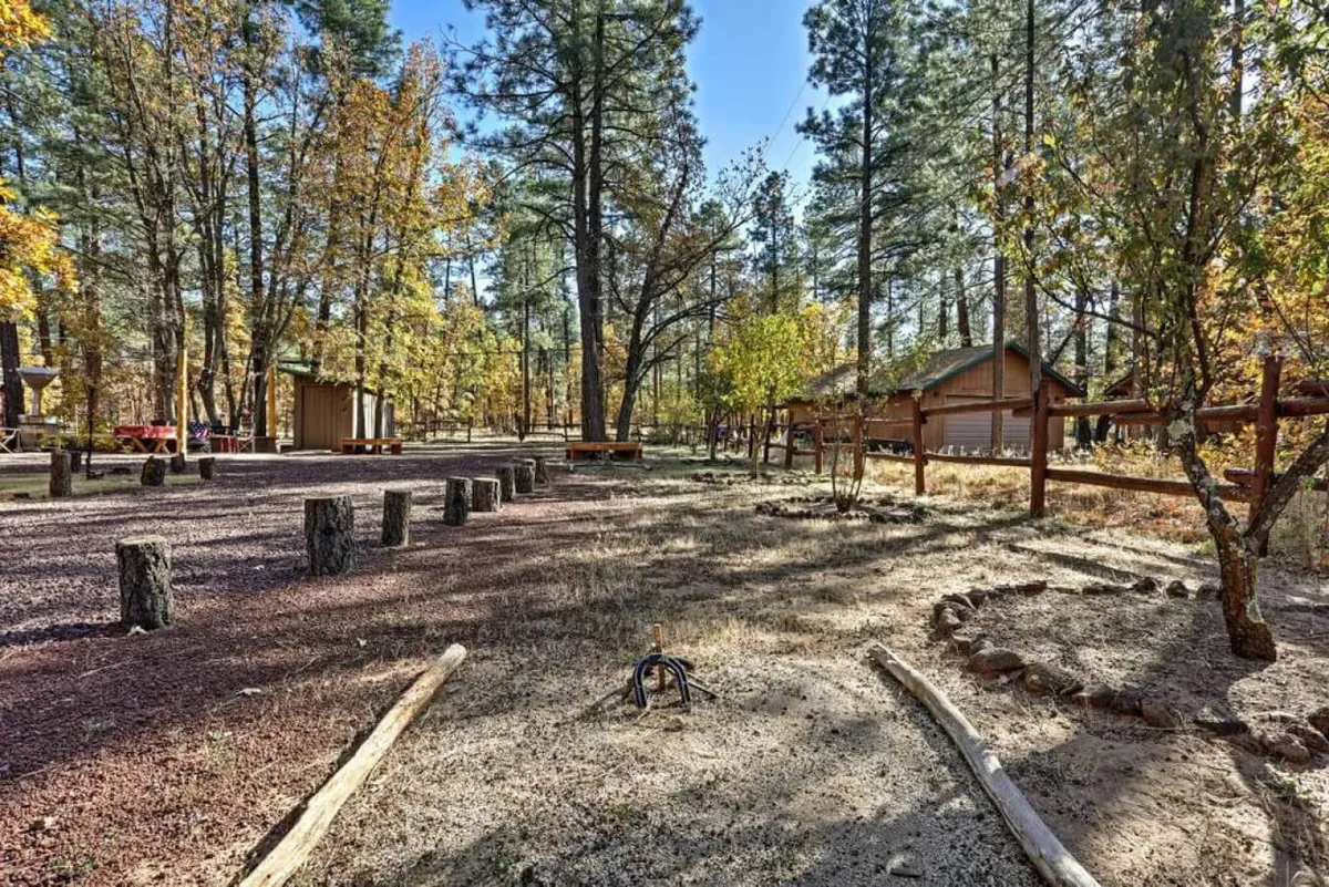 This image features an inviting outdoor seating area centered around a fire pit, bordered by a tree line and connected by a winding pathway. The space suggests areas for picnicking or relaxing and is ideal for gatherings under the open sky. The arrangement is spacious, making it suitable for both adults and children to enjoy safely.